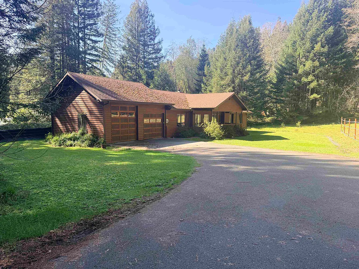 Front exterior of 1500 Tolowa Rd — a custom-built all-wood home with a horse-shoe driveway, set against a stand of redwoods.